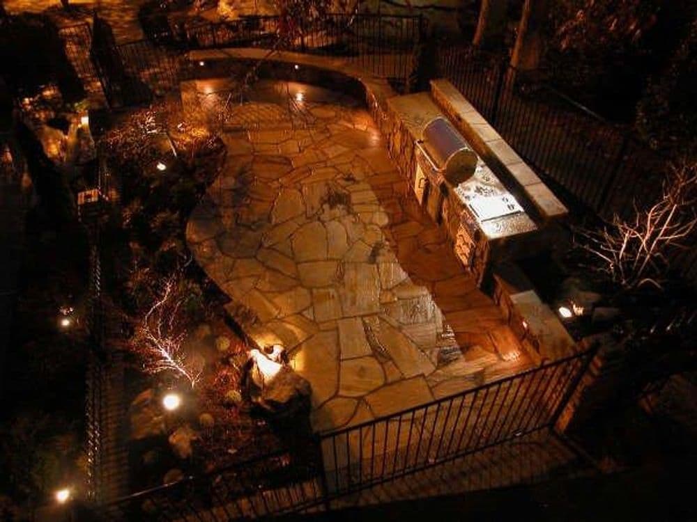 Elegant outdoor patio with stone flooring, a barbecue area, and soft evening lighting.