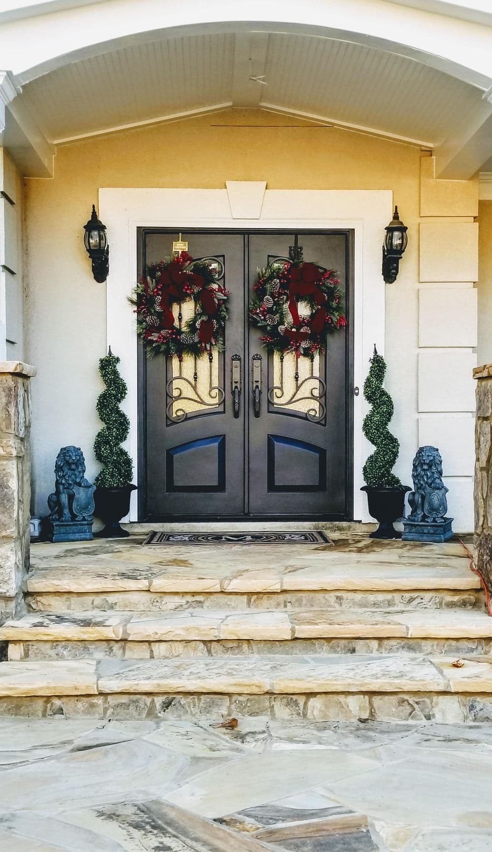 Elegant double front doors adorned with wreaths, flanked by topiary and lion statues.