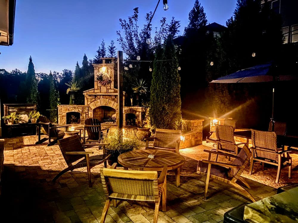 Cozy outdoor patio with stone fireplace, seating area, and string lights at dusk.