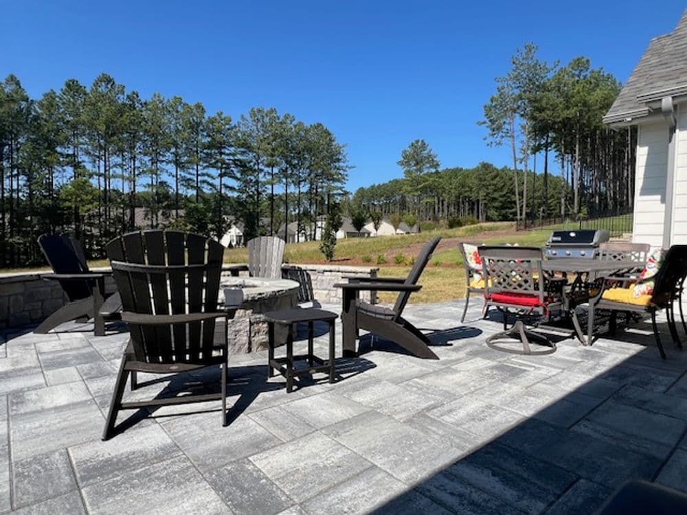 Outdoor patio with black chairs, stone table, and lush forest backdrop under a clear blue sky.