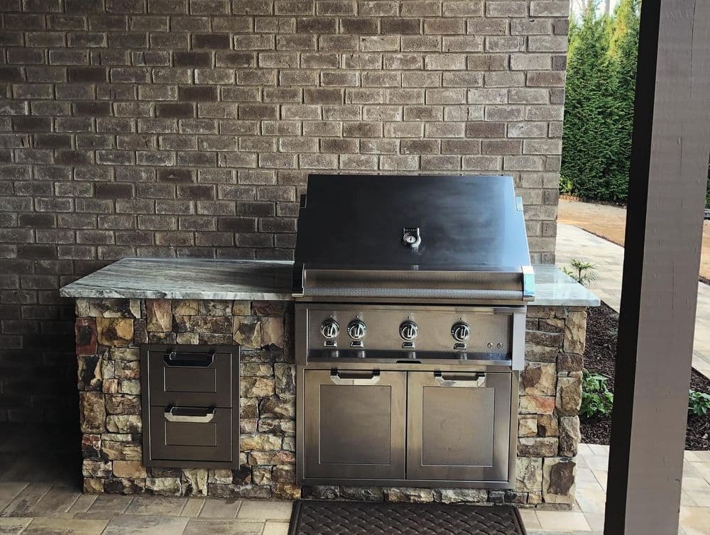 Outdoor kitchen featuring a stainless steel grill with stone countertop and cabinetry.
