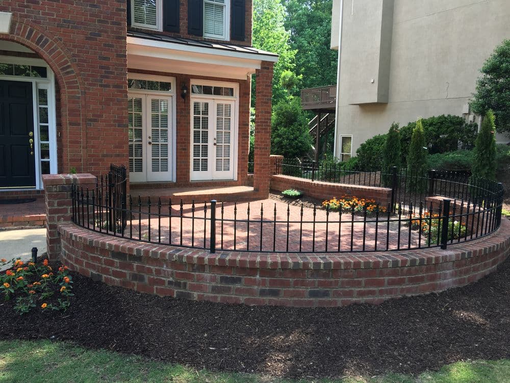 Brick front porch with black iron railing, flower beds, and decorative landscaping.